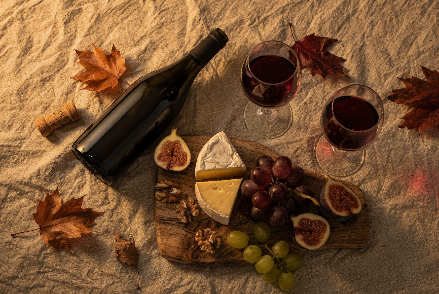 Bouteille de vin rouge, deux verres et planche de fromages, noix et figues sur une table d’automne